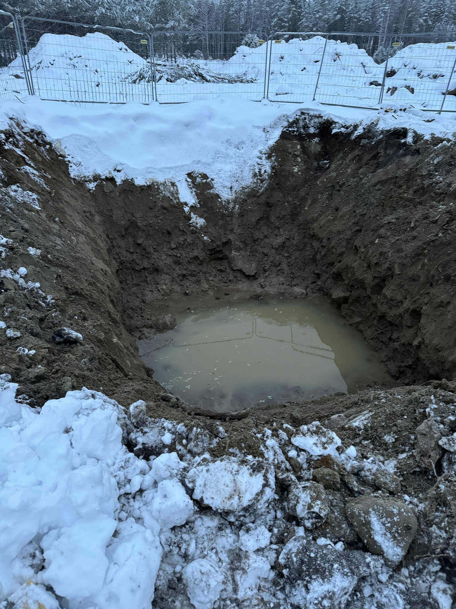 Vatten i en snötäckt schakt för kraftledningsfundament