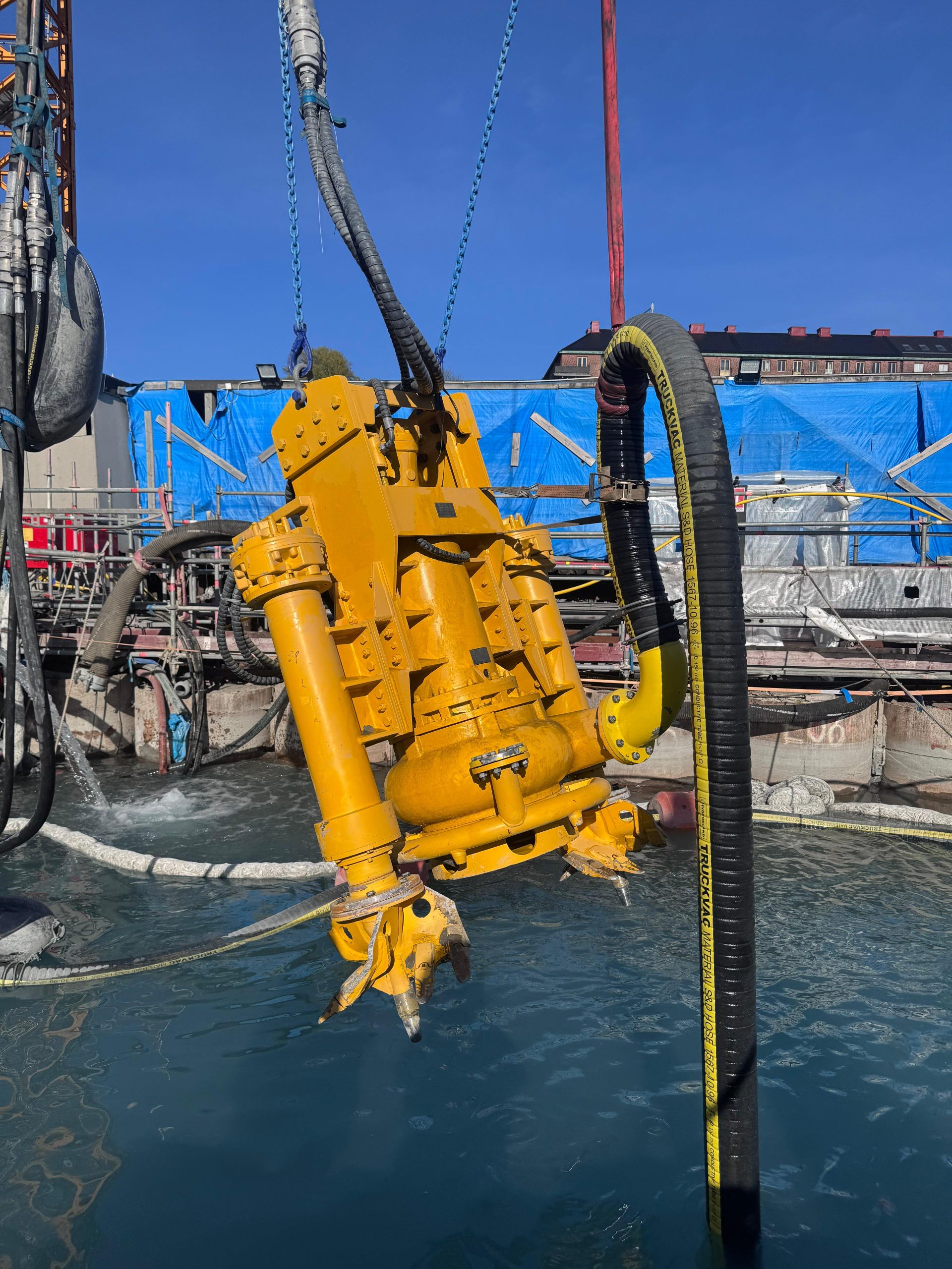 Gul hydraulisk mudderpump lyfts över vatten på arbetsplatsen